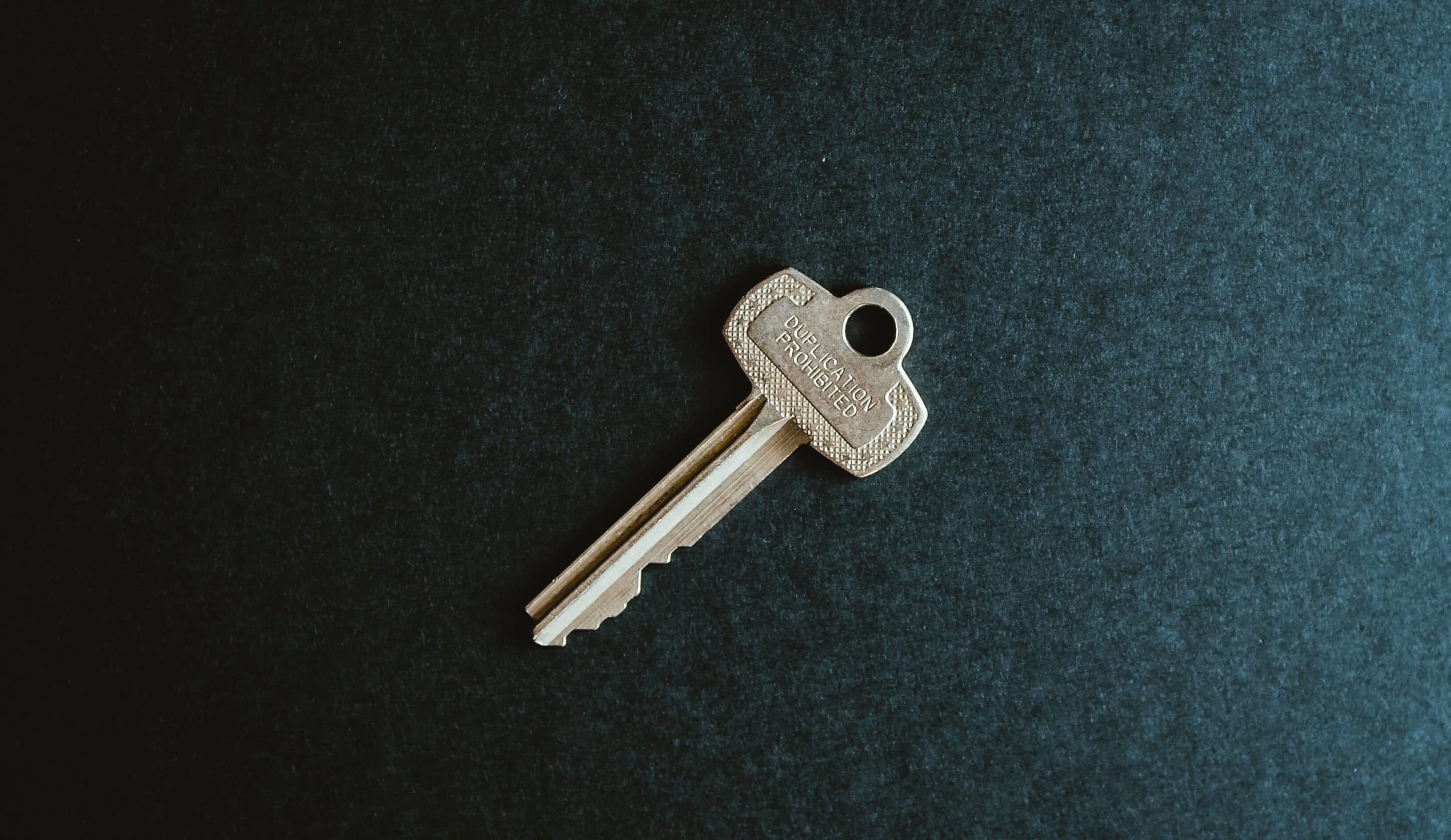A house key sitting against a dark navy backdrop.
